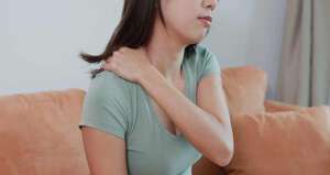 Frau hebt sich die Hand auf die Schulter wegen der Schmerzen